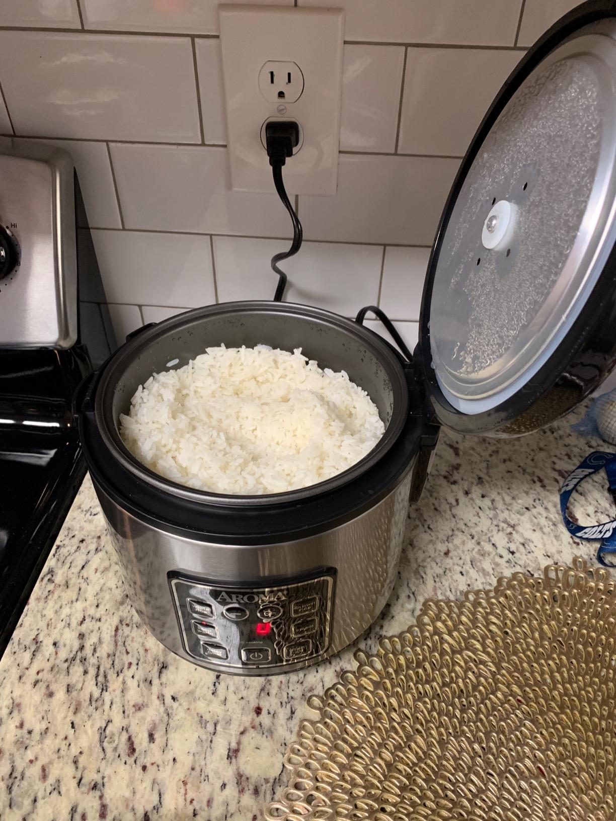 Rice cooker connected  a room  counter, lid open, revealing cooked achromatic  atom   inside