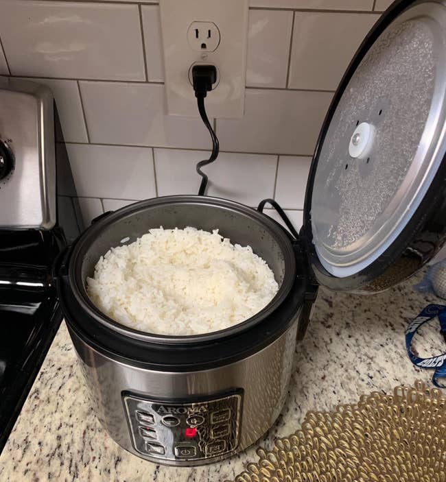 Rice cooker connected a room counter, lid open, revealing cooked achromatic atom inside