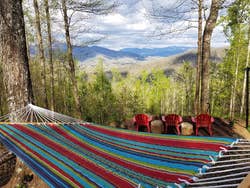 The striped hammock hung between two trees in front of a view of forest and mountains