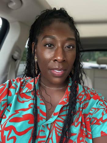 Person in a floral-patterned shirt is seated in a car, looking at the camera with a neutral expression