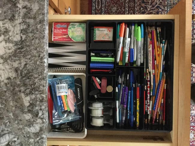 The desk drawer organizer in a customer's drawer, full of markers, pens, and miscellaneous items