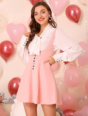 a model in a light pink pinafore dress with suspenders