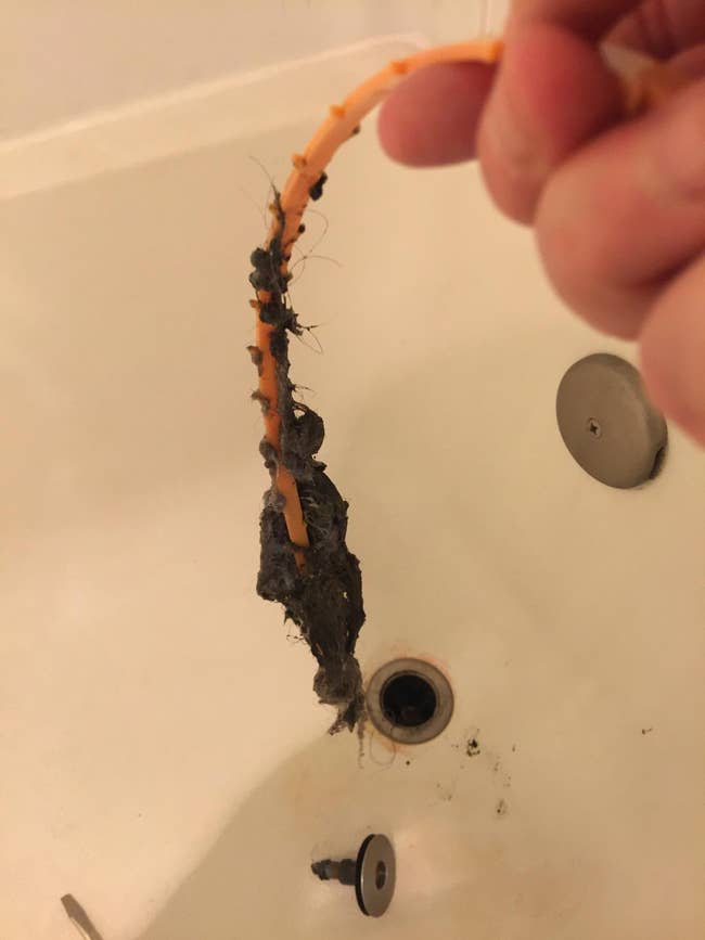 reviewer pulling a gross glob of hair from their drain with the tool