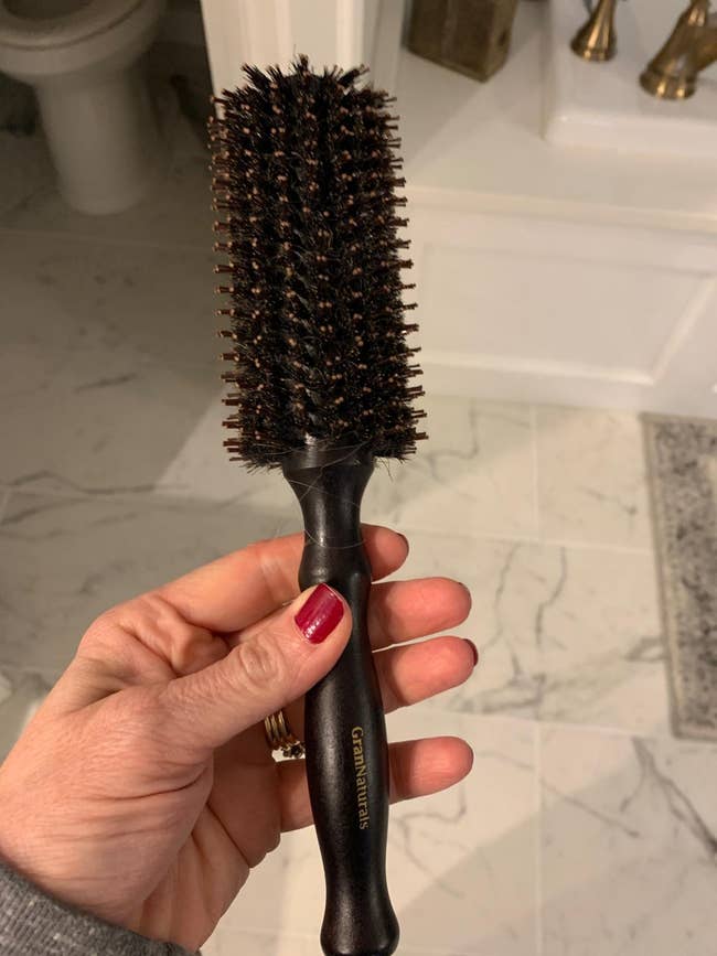 Person holding a bristle hairbrush with a black handle