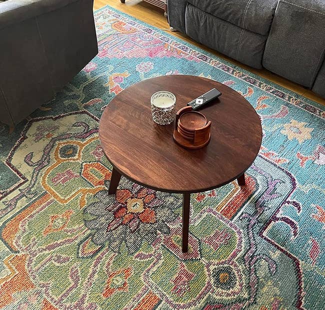 circular wooden coffee table with a candle, remote, and coaster set on top