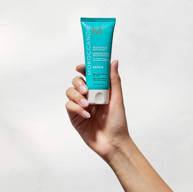 Hand holding a conduit of Moroccanoil Restorative Hair Mask, highlighting hairsbreadth repair benefits, perfect for nonfiction categorized arsenic Shopping