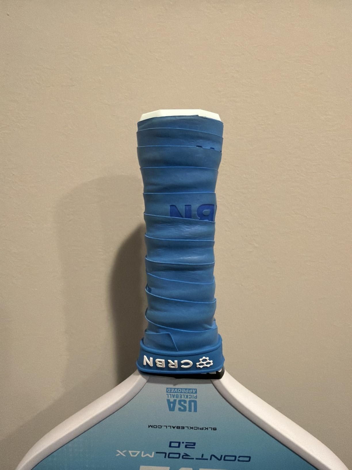 Close-up of a pickleball paddle grip  with a bluish  grip, showing branding and 
