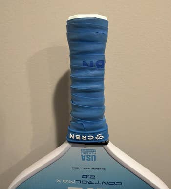 Close-up of a pickleball paddle grip with a bluish grip, showing branding and