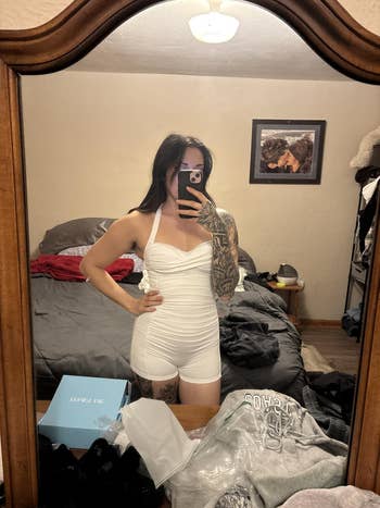 Person successful a achromatic romper taking a reflector selfie successful a bedroom, showcasing a buying item