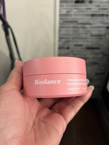 A hand holds a container of Biodance collagen peptide eye patches, with packaging details in English and French