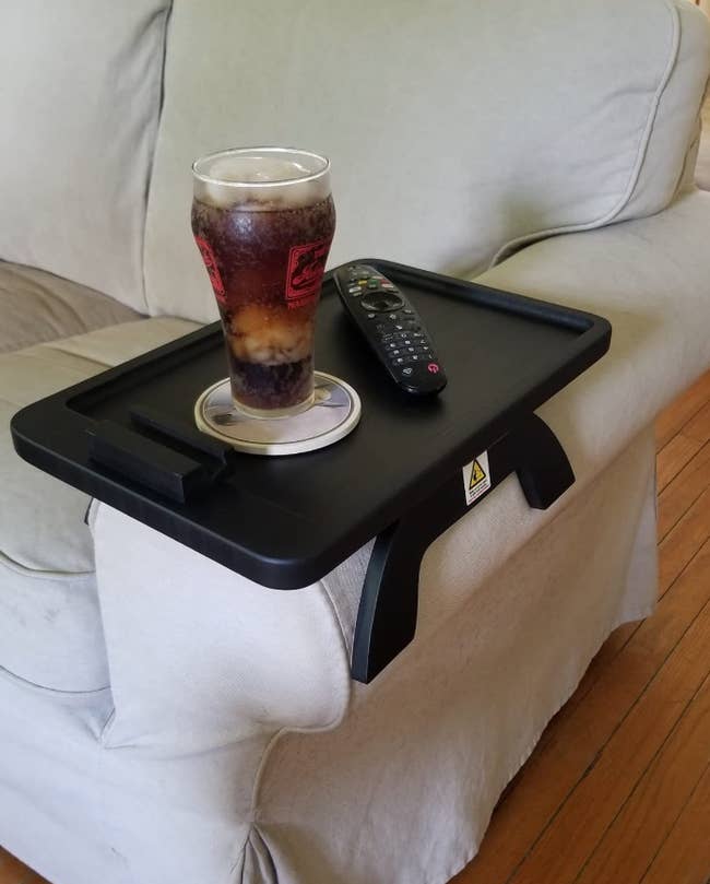 reviewer's sofa table resting on arm est with drink and remote on top