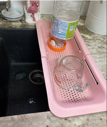 pink rectangular colander set atop a sink with dishes drying on it 