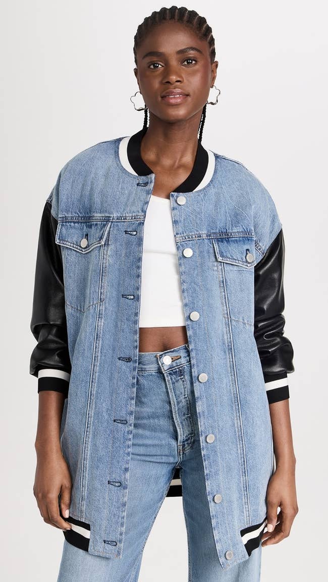 model in long light denim jacket with black faux leather sleeves and white athletic strip trim