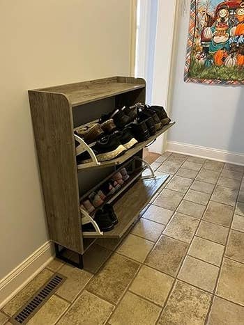 Freestanding footwear  rack with 2  tilted shelves holding assorted  pairs of shoes successful  a tiled hallway