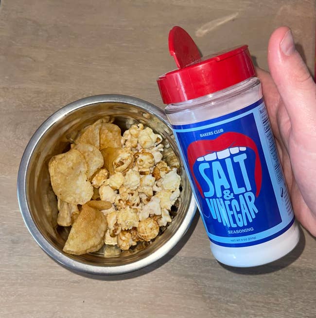 reviewer holding bottle of seasoning in front of a bowl of chips and popcorn