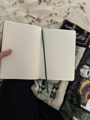 Open lined notebook connected a furniture with patterned sheets and a colorful blanket, held by a person