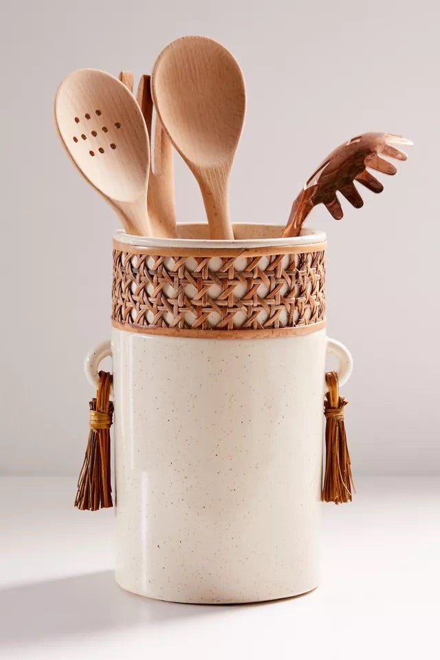 Speckled ceramic utensil holder with brown tassels and a brown straw pattern wrapped around the holder