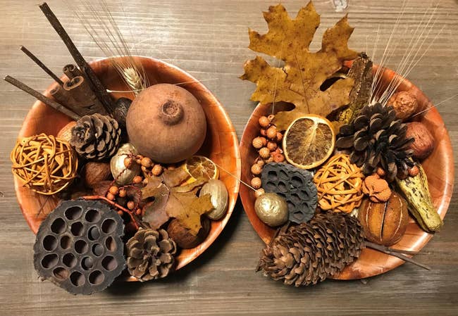 Two decorative bowls filled with dried pinecones, leaves, lotus pods, and citrus slices, arranged for an autumn-themed display