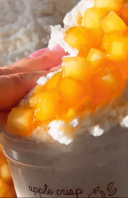 Close-up of a manus  holding an pome  crisp parfait topped with diced apples and whipped cream. The substance   