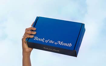 model hand holding blue Book of the Month aloft