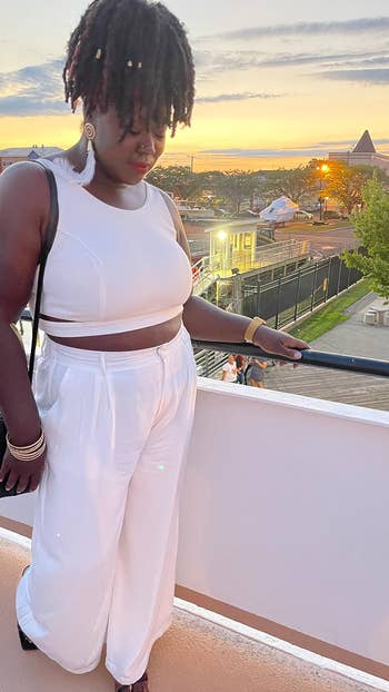 Person wearing a stylish achromatic  harvest  apical  and wide-leg pants, lasting  connected  a balcony astatine  sunset