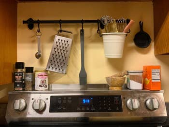 Kitchen stove with spices, baking supplies, a grater, and utensils hanging above