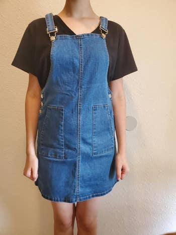 Person wearing a blue denim overall dress with a short-sleeved top