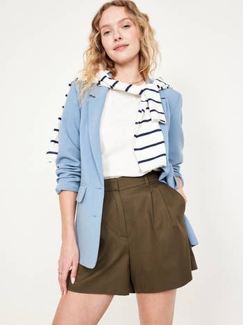 Woman wearing a blue blazer, striped scarf, white top, and olive shorts