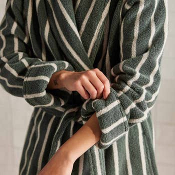 Model rolling up   sleeve of a acheronian  greenish  and white-striped bathrobe, showcasing the thick, lush material