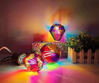 Gem-shaped and spherical decorative lights emit vibrant patterns, illuminating a country beside a tiny potted plant, creating a cozy ambiance