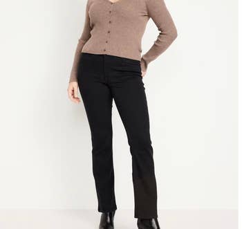 A person is wearing a button-up cardigan and black, straight-cut pants with ankle boots, posing against a plain background
