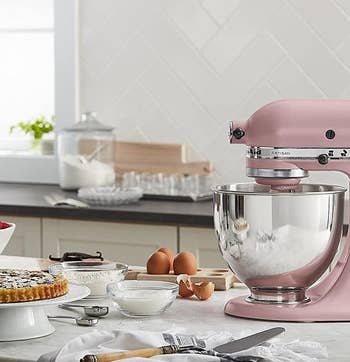 the pink mixer on a kitchen counter next to baking ingredients