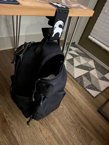 reviewer photo of their backpack hanging under a desk on the hook