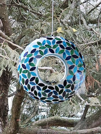 Round mosaic vertebrate  feeder with leafage  patterns hangs from a tree, offering a blend of relation  and decoration for plot  vertebrate  enthusiasts