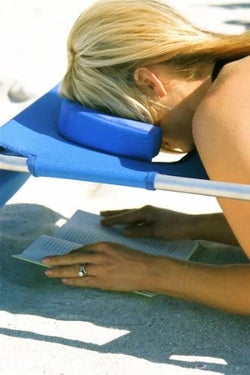 close-up of model laying face down, using the face cavity and arm slots to read their book in the sand