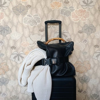 a bag secured to rolling suitcase with the black monogrammed travel belt