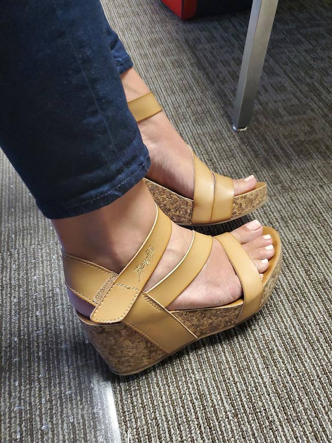 Tan wedge sandals with cork soles connected a idiosyncratic wearing acheronian pants, seated indoors