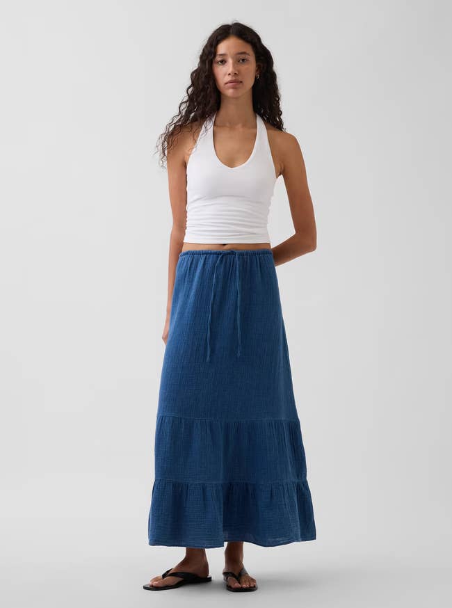 Person modeling a casual outfit with a achromatic  halter apical  and a agelong  bluish  tiered skirt, suitable for relaxed summertime  shopping