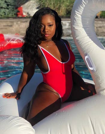 reviewer wearing one piece in red while on a swan floatie