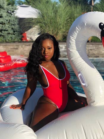 reviewer wearing one piece in red while on a swan floatie