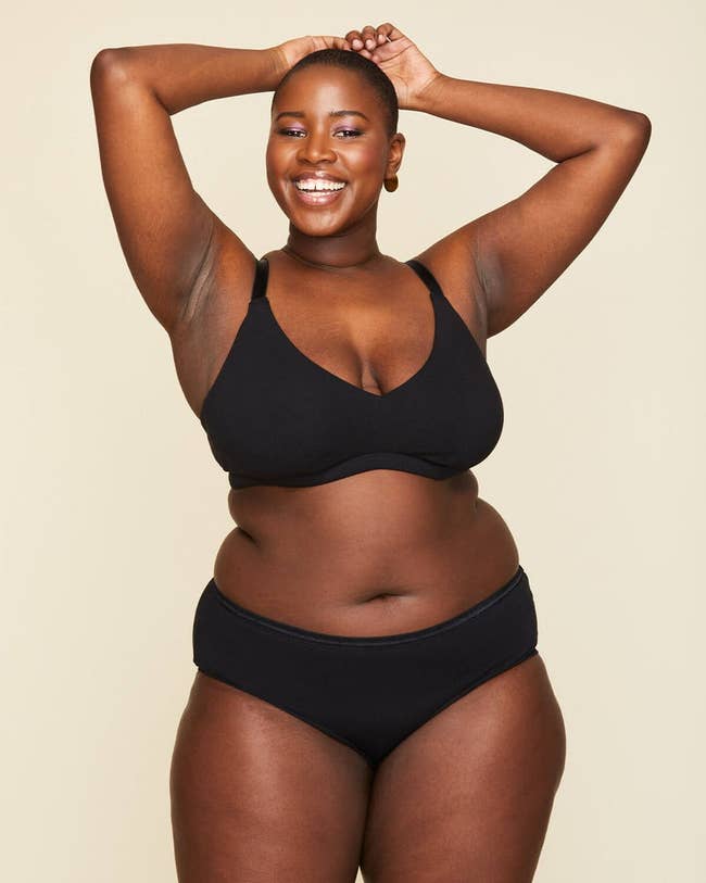 model smiling in a black bra and panties, posing with her hands behind her head