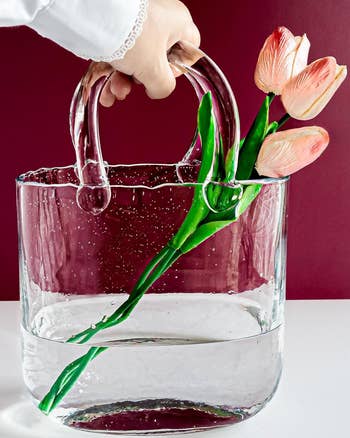 Hand placing tulips into a clear glass purse vase 