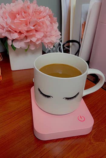 reviewer's eyelash coffee cup sitting on the pink mug warmer