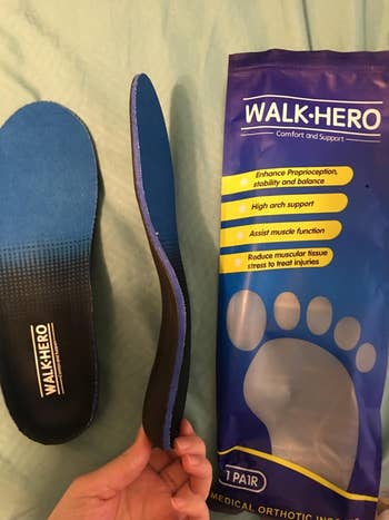 A reviewer holds a foot insole next to its packaging, highlighting the product's arch support