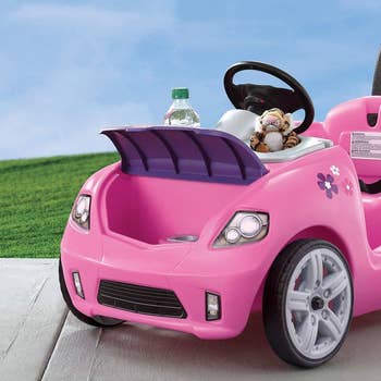 Toy car in pink with a water bottle and stuffed toy on grass and pavement