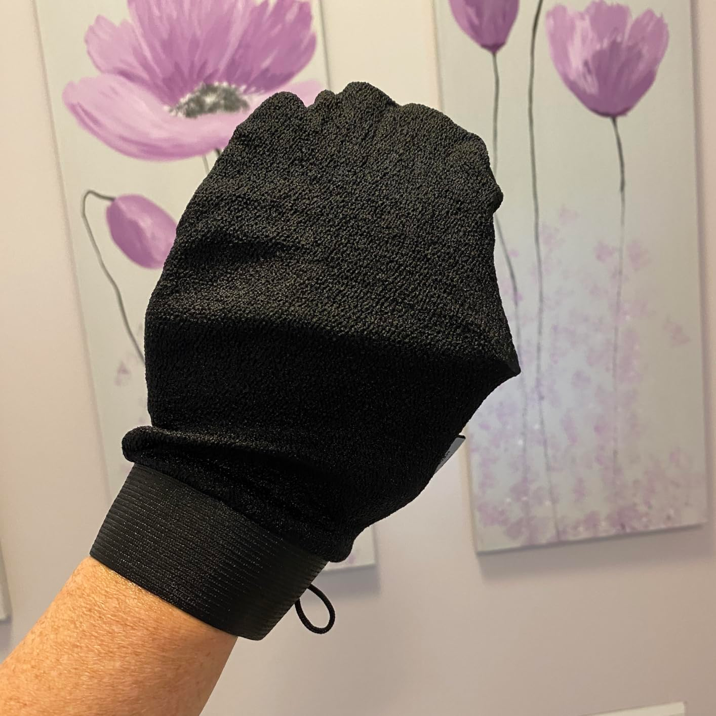 Exfoliating mitt  for skincare displayed, held by a person's hand, with floral artwork successful  the background