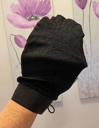 Exfoliating mitt for skincare displayed, held by a person's hand, with floral artwork successful the background