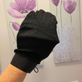 Exfoliating glove for skincare displayed, held by a person's hand, with floral artwork in the background