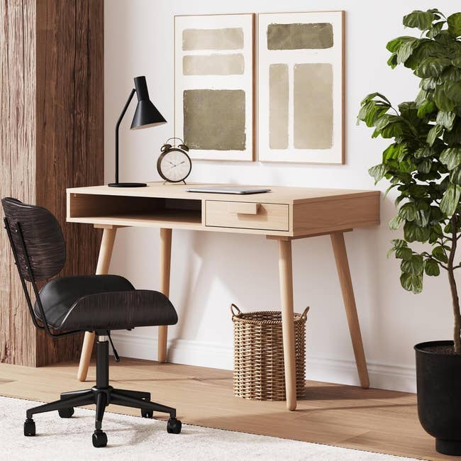 Modern home office setup with a wooden desk, chair, table lamp, clock, and decorative plant, ideal for a stylish work or study space