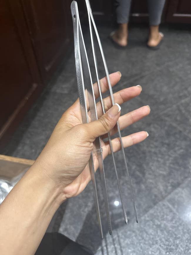 Hand holding 4  agelong  metallic  skewers successful  a room  setting, with a furniture  disposable   successful  the background